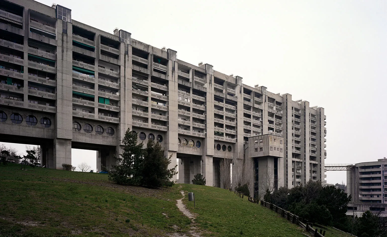 A long brutalist housing block on a grassy hill